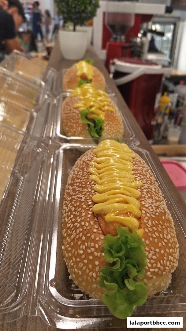 Three sesame seed buns with mustard and lettuce, packaged in clear plastic containers.
