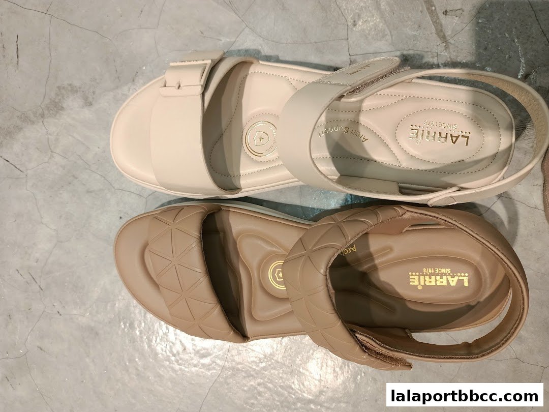A pair of stylish Larrie sandals in beige and cream colors displayed on a concrete floor.