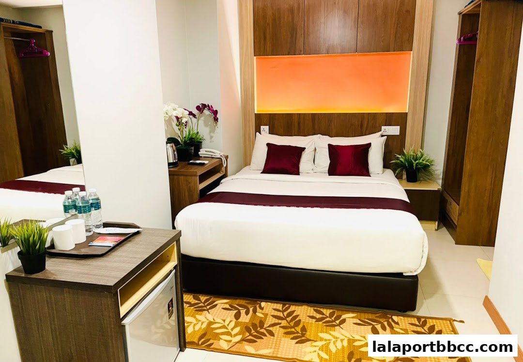 A hotel room featuring a neatly made bed with burgundy accents and a bedside table with amenities.