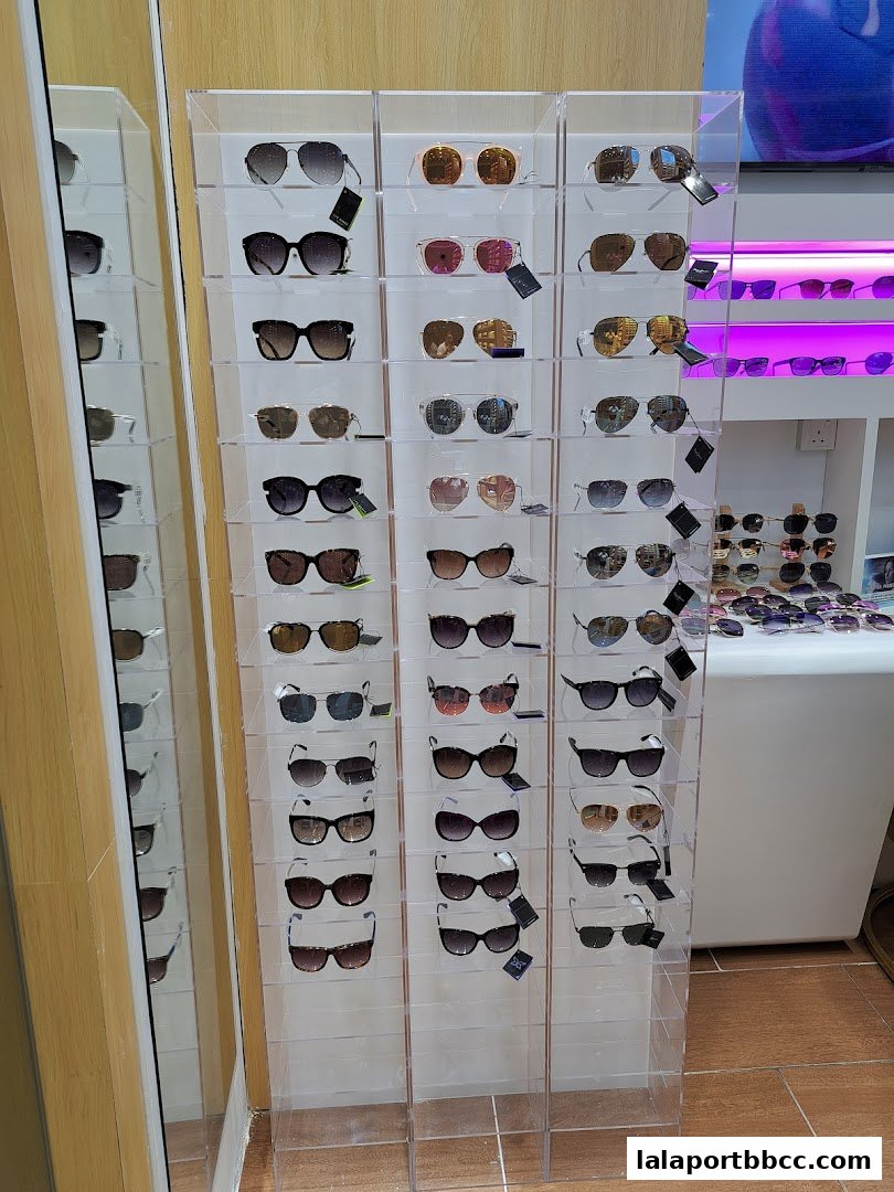 A display of various sunglasses on clear acrylic shelves, with a mirror reflecting more eyewear.