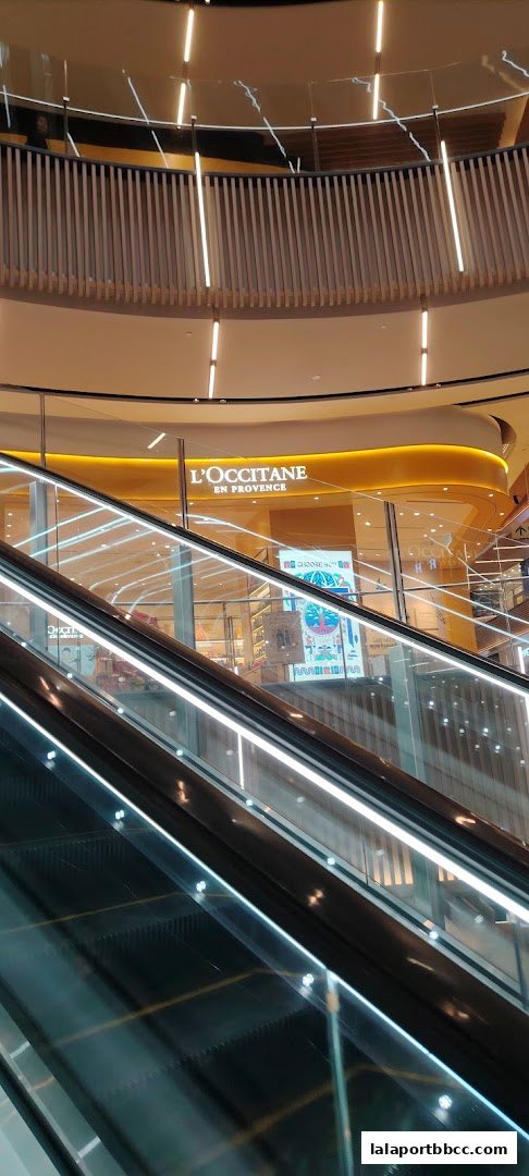 The L'Occitane En Provence shop front is visible from an escalator in a modern shopping mall.