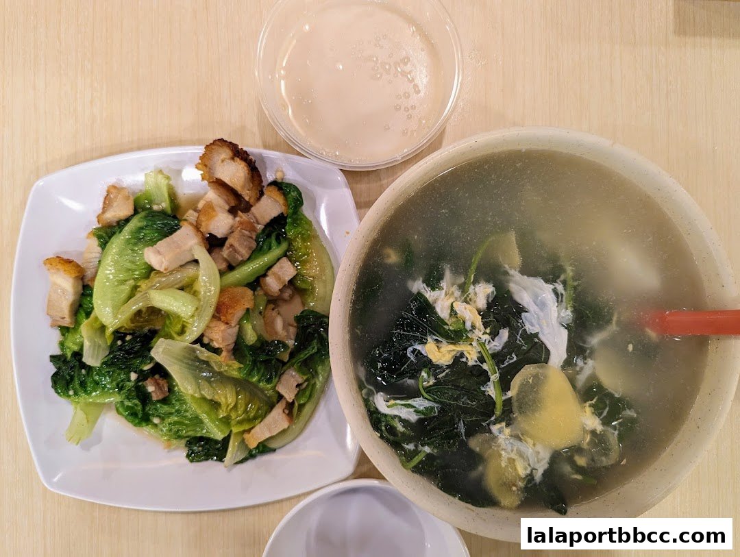 A top-down view of a meal featuring stir-fried vegetables with pork and a bowl of soup.