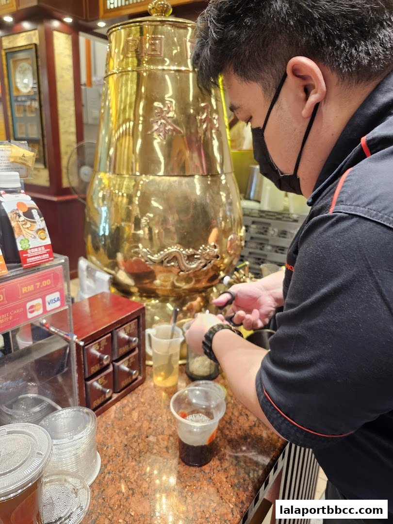 A staff member prepares a drink at a counter with a large golden dispenser.