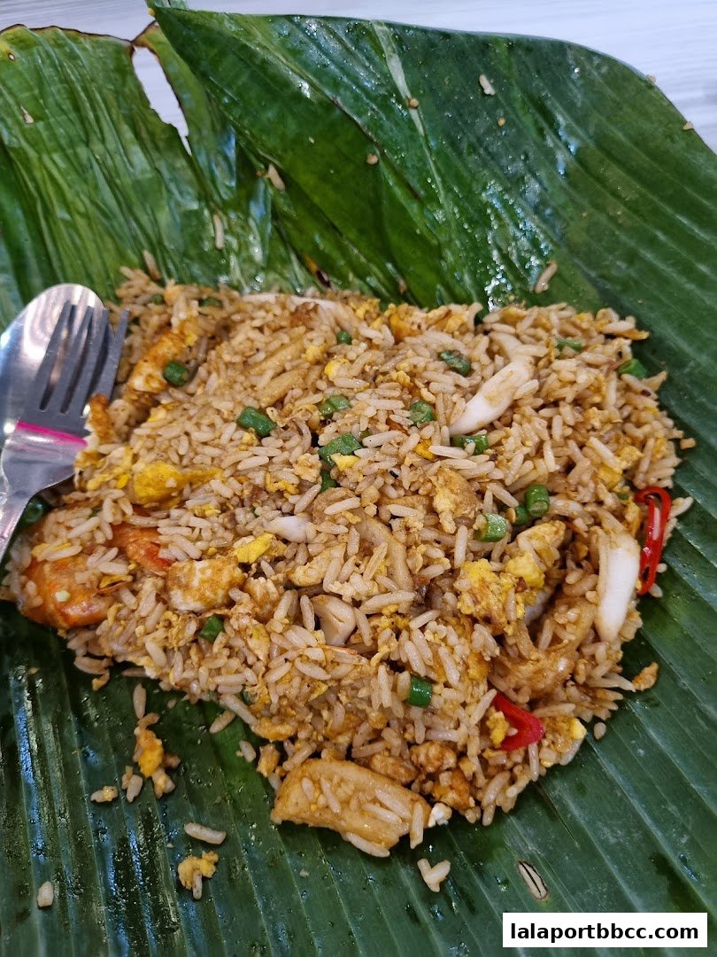 A plate of seafood fried rice served on a banana leaf with a fork and spoon.