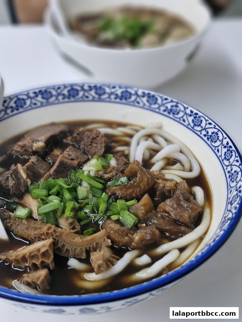 A close-up of a bowl of Hong Kong-style noodles with beef and tripe, garnished with green onions.