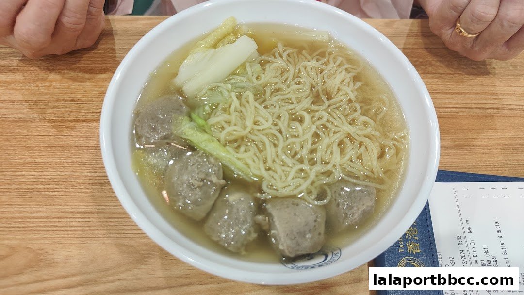 A bowl of Hong Kong-style noodle soup with meatballs and vegetables, next to a receipt.