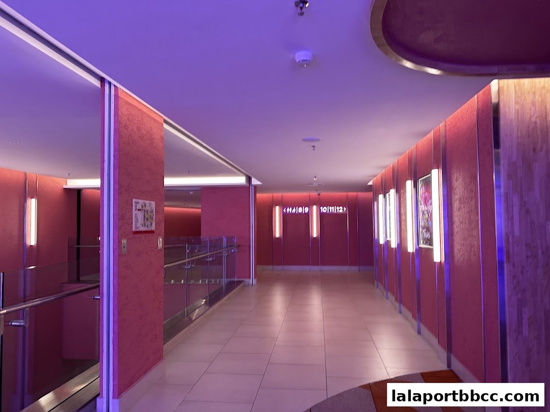 A modern hallway with pink walls, illuminated by vertical lights and featuring numbered doors.