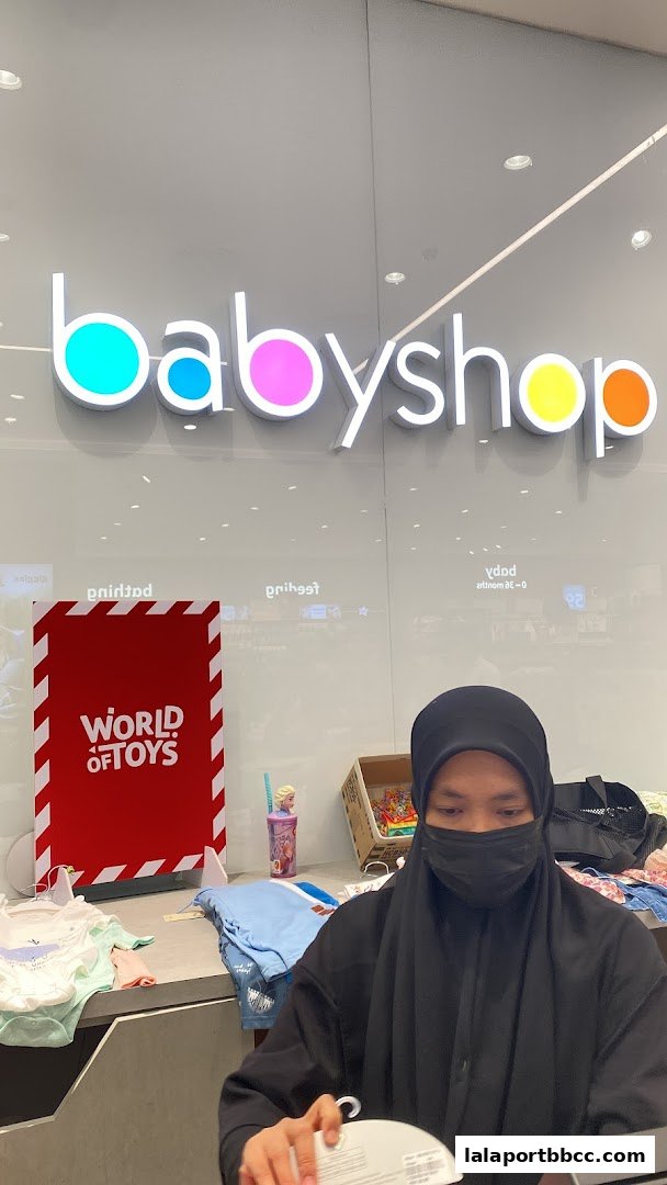 A person in a black hijab and mask stands behind a counter at Babyshop.