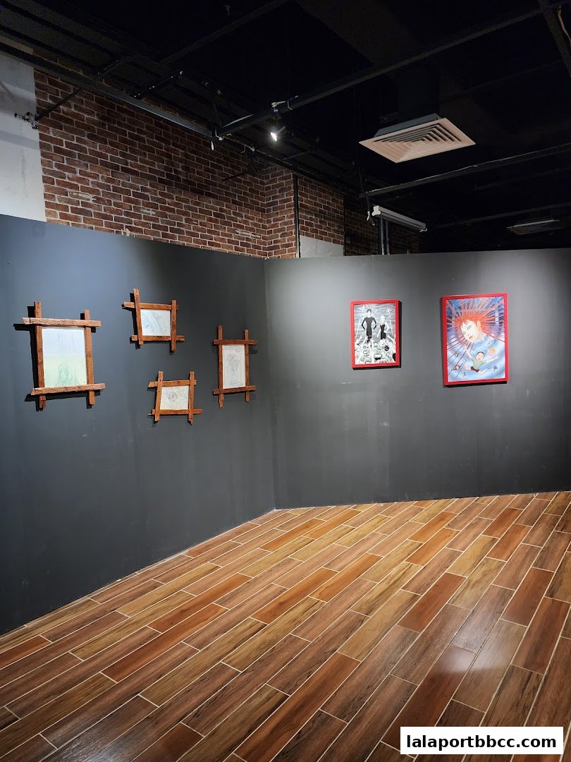 An art exhibition space with framed artwork displayed on a dark grey wall.