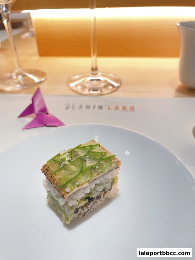 A meticulously crafted dish with layers of ingredients, topped with cucumber slices and a delicate flower.