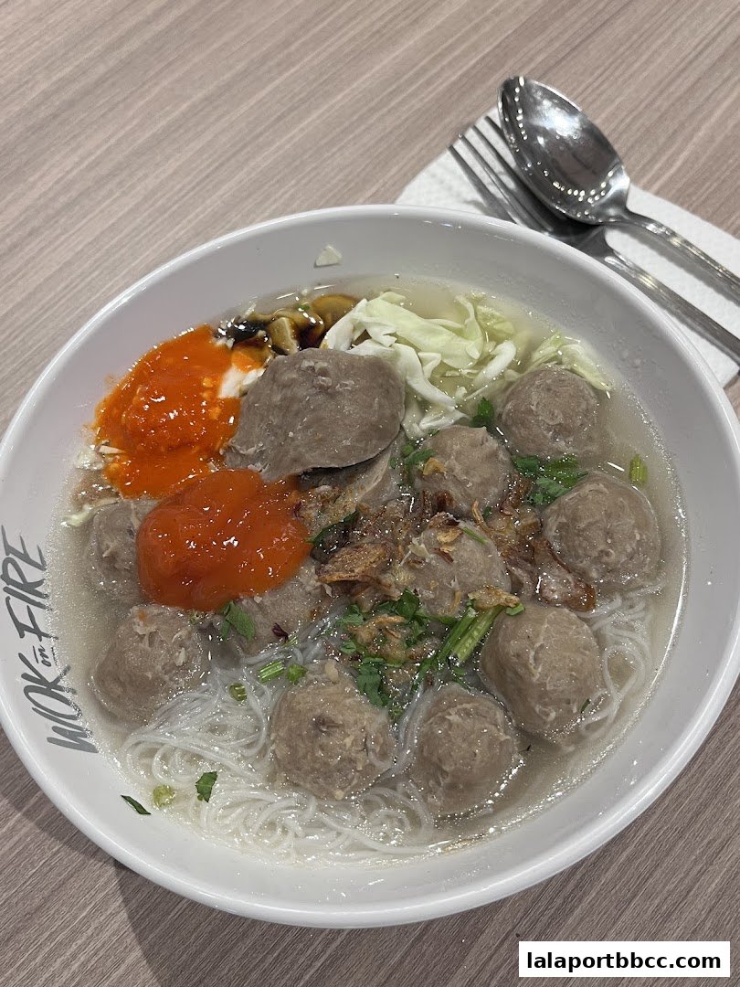 A bowl of delicious meatball soup with noodles, chili sauce, and cabbage.