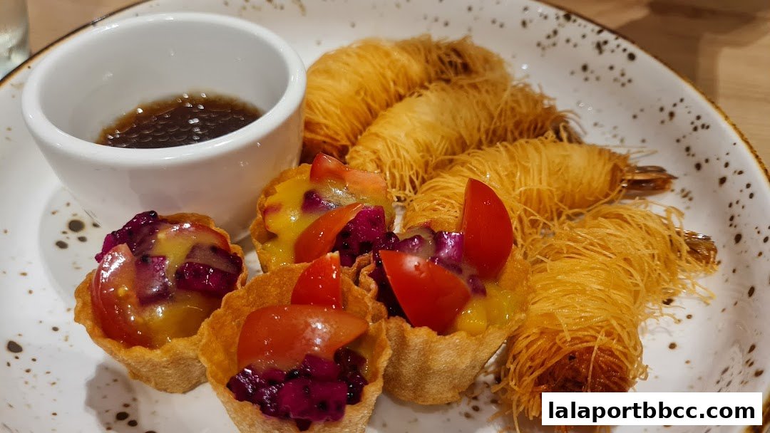 A plate of appetizers featuring crispy fried shrimp and small tarts with fruit and tomato toppings.