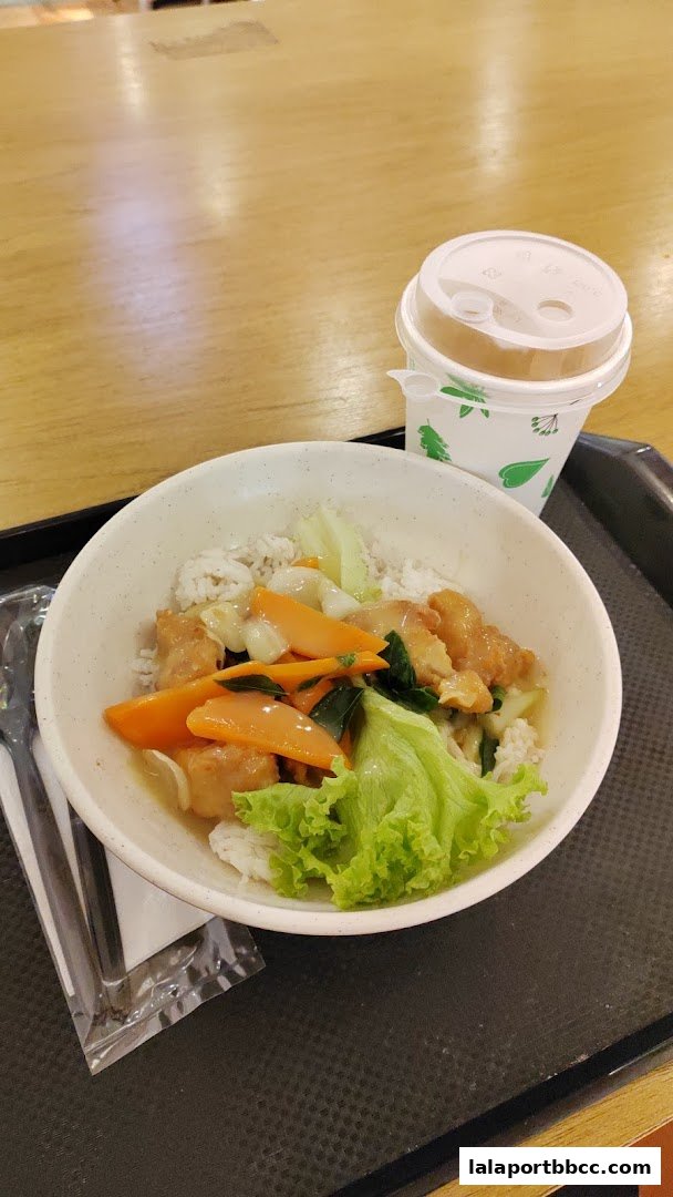 A bowl of fried rice with vegetables and a drink on a tray.