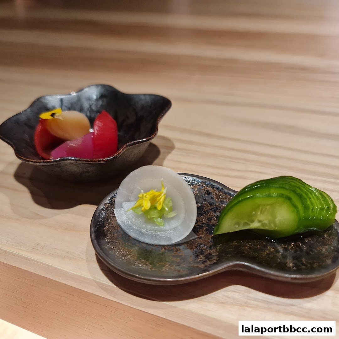 Artfully presented pickled vegetables and cucumber slices on dark ceramic plates.