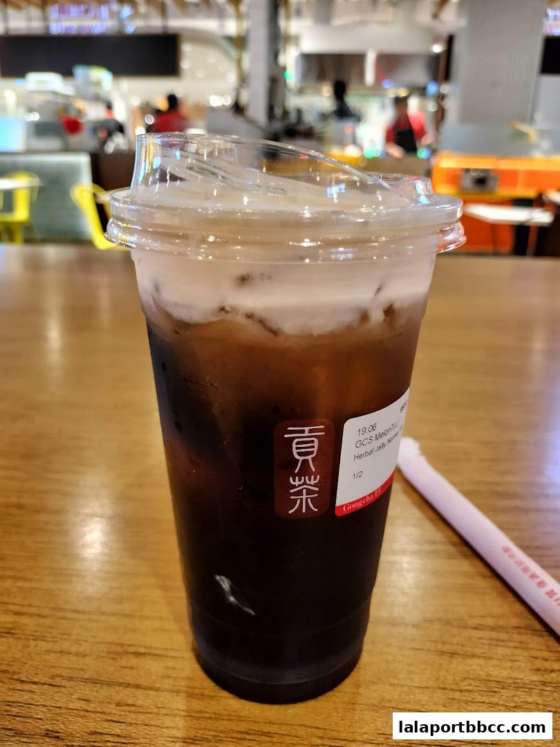 A close-up of a Gong Cha drink with a creamy topping and a straw on a wooden table.
