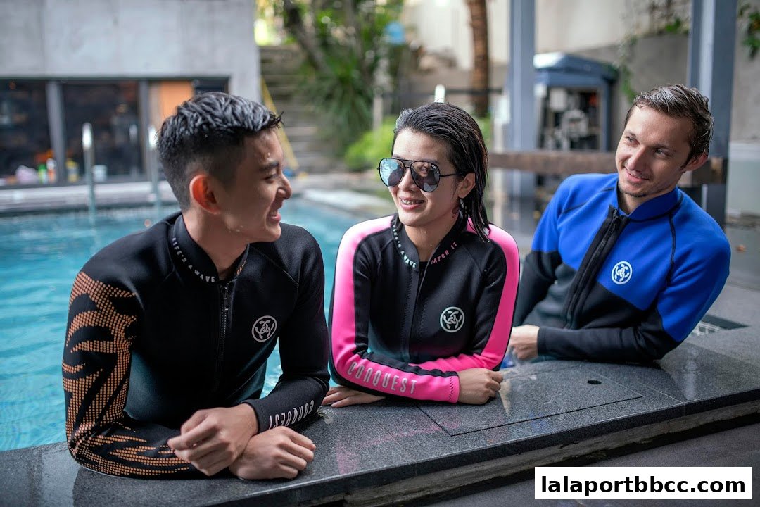 Three people in wetsuits smiling and talking by a pool.
