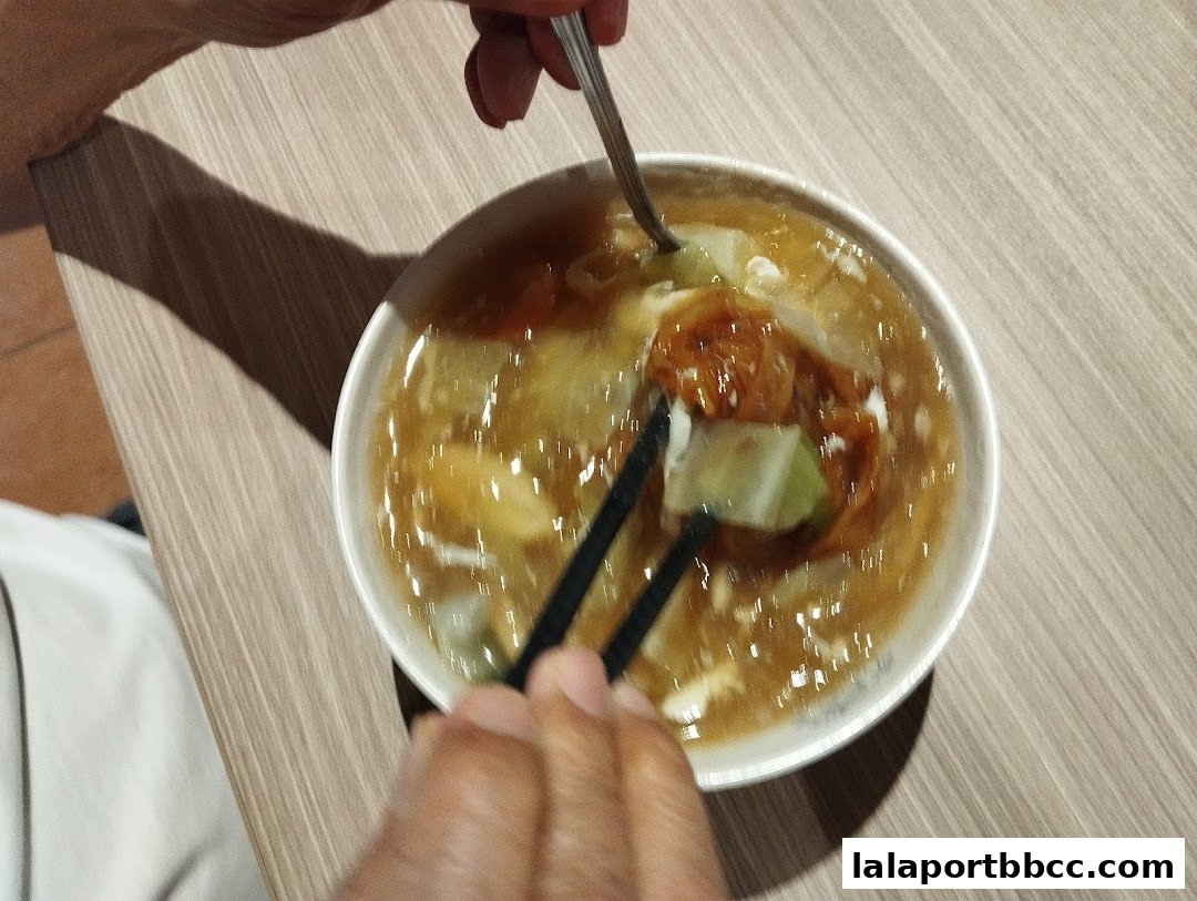A close-up shot of a person eating a bowl of Hokkien Mee with chopsticks and a spoon.