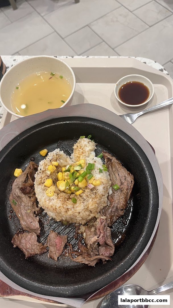 A sizzling claypot dish with rice, beef, corn, and a side of soup and dipping sauce.