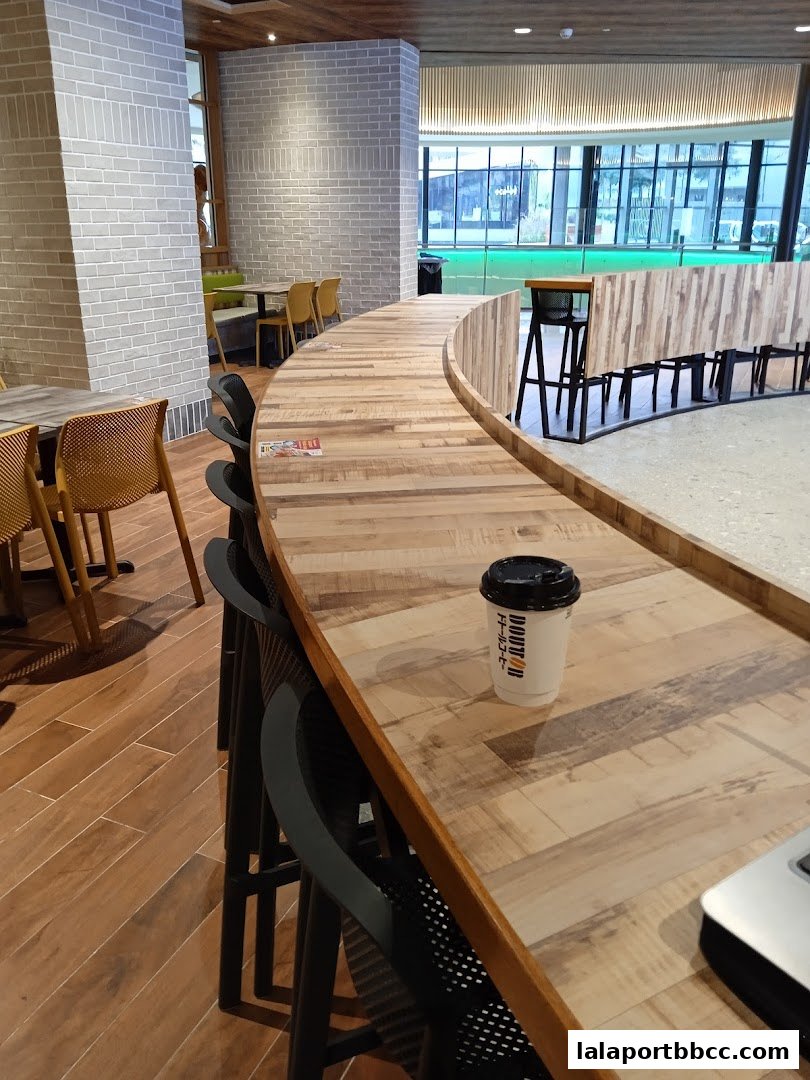 A coffee cup sits on a wooden counter in a modern cafe with brick walls and seating.