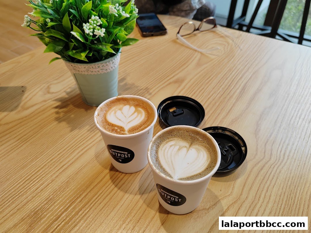 Two cups of coffee with latte art on a wooden table, next to a potted plant.