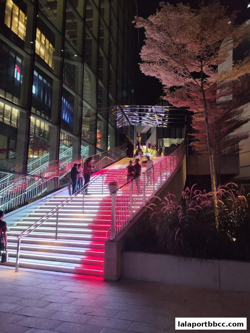 People ascend illuminated stairs at night outside a modern building with glass facade.