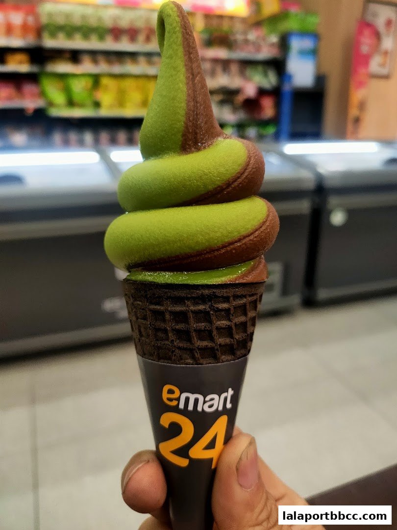 A hand holds a dual-flavored soft-serve ice cream cone with a chocolate waffle cone.