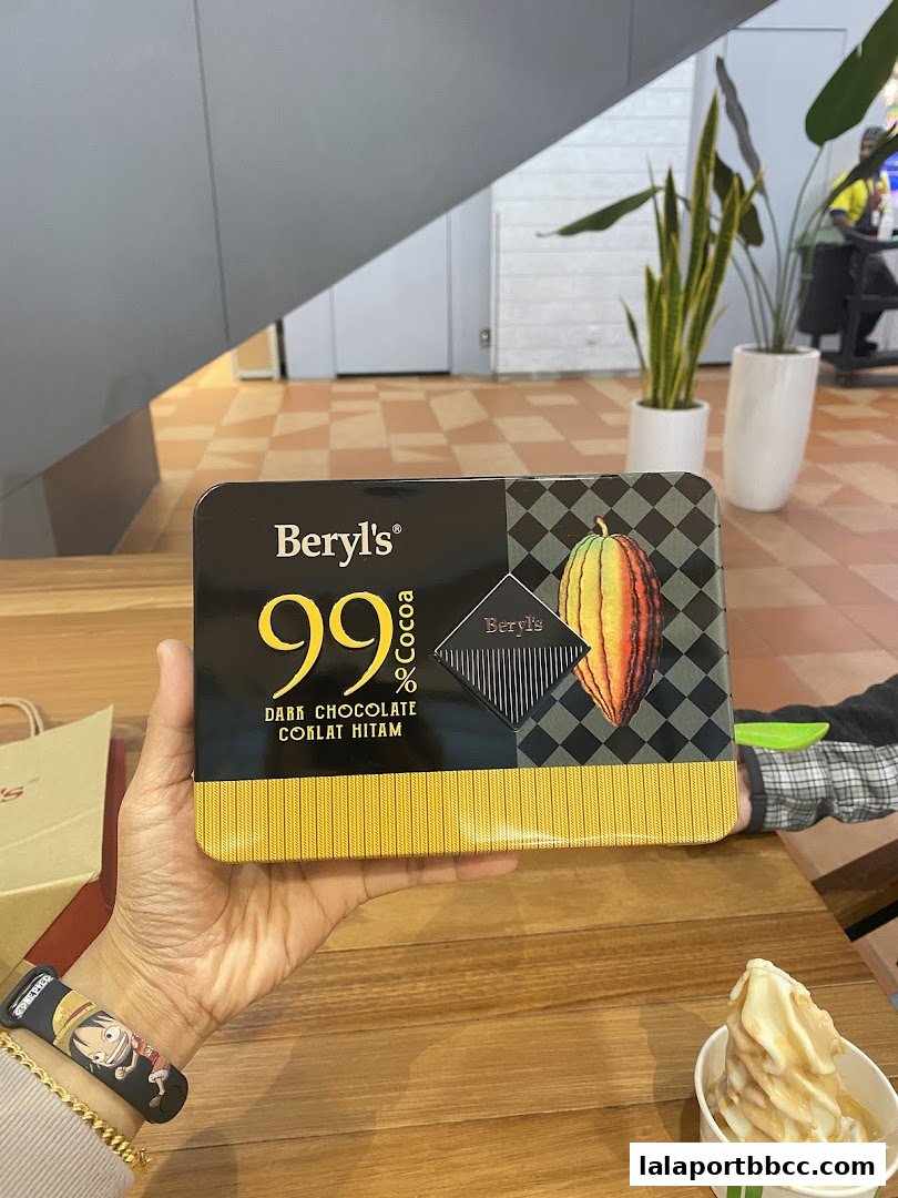 A hand holds a box of Beryls 99% Dark Chocolate next to a soft-serve ice cream.