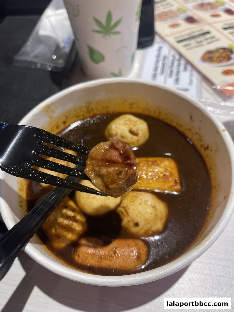 A fork lifts a meatball from a bowl of savory broth with various ingredients.