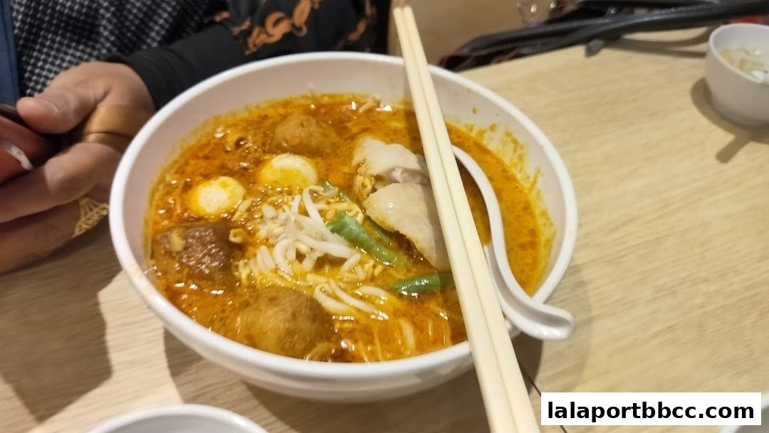 A close-up shot of a delicious bowl of curry laksa with chicken, fish balls, and bean sprouts.