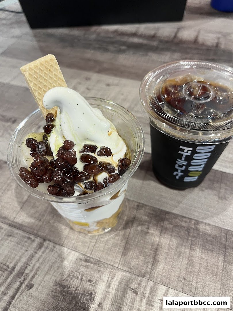 A parfait with soft serve ice cream, red beans, and a wafer, next to a cup of iced coffee.