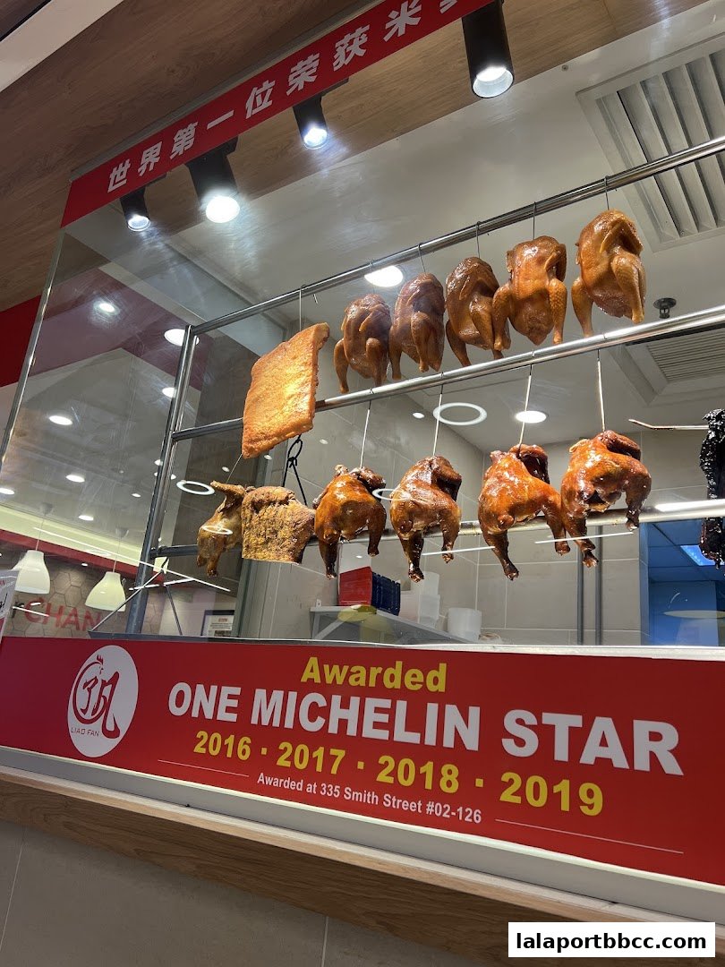 A display of roasted chickens and pork belly hanging in front of a restaurant window.