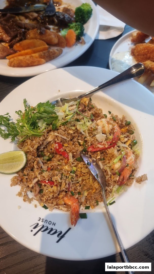 A plate of fried rice with shrimp, vegetables, and a lime wedge, with other dishes blurred in the background.