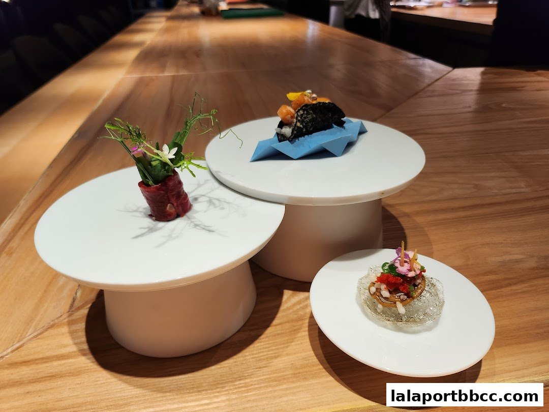 Three artfully presented small dishes with fresh ingredients and garnishes on white platters.