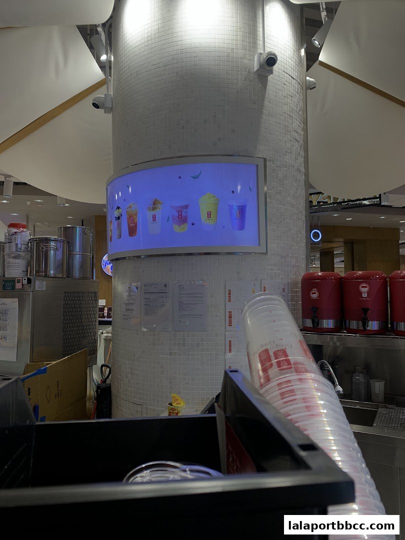 A display screen shows colorful drinks at Gong Cha Lalaport BBCC, with cups stacked in the foreground.