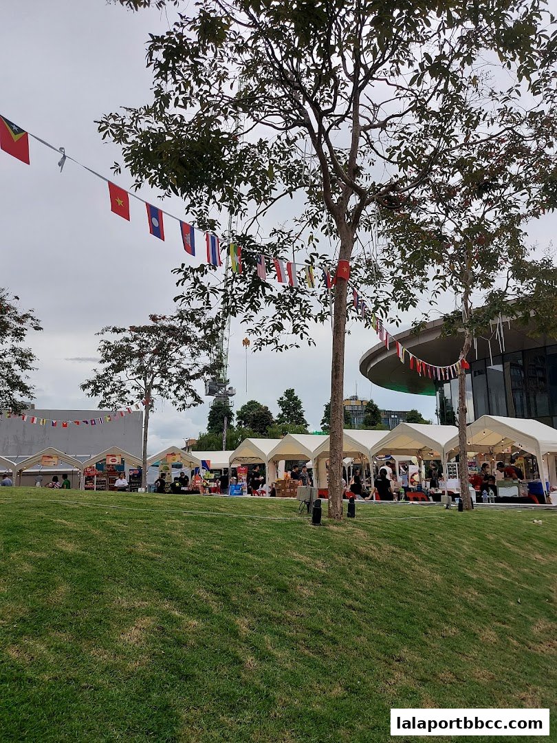 Outdoor market stalls with international flags strung between trees and a grassy hill.