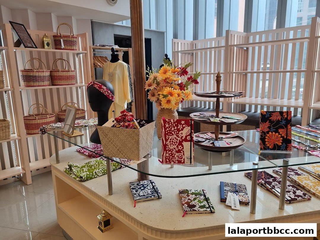 A retail display featuring batik-patterned notebooks, baskets, and clothing, with decorative flowers.