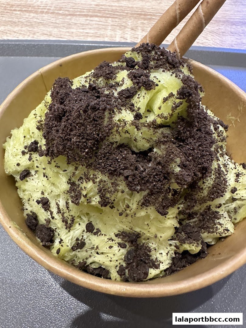 A bowl of shaved ice dessert topped with crushed cookies and two wafer sticks.