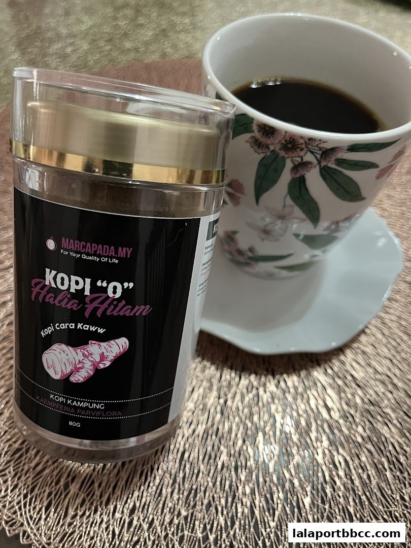 A container of Kopi 'O' Halia Hitam coffee next to a floral patterned cup of coffee.