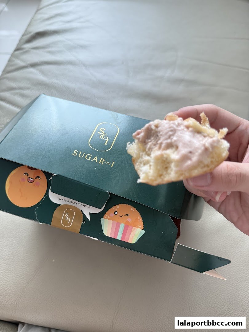 A hand holds a bite of a pastry from a Sugar and I branded box.