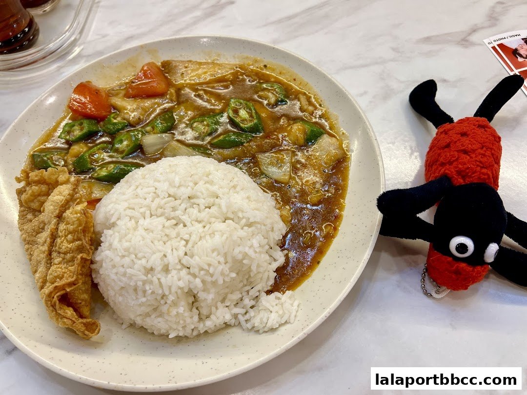 A plate of rice with curry and fried fish, next to a stuffed toy.