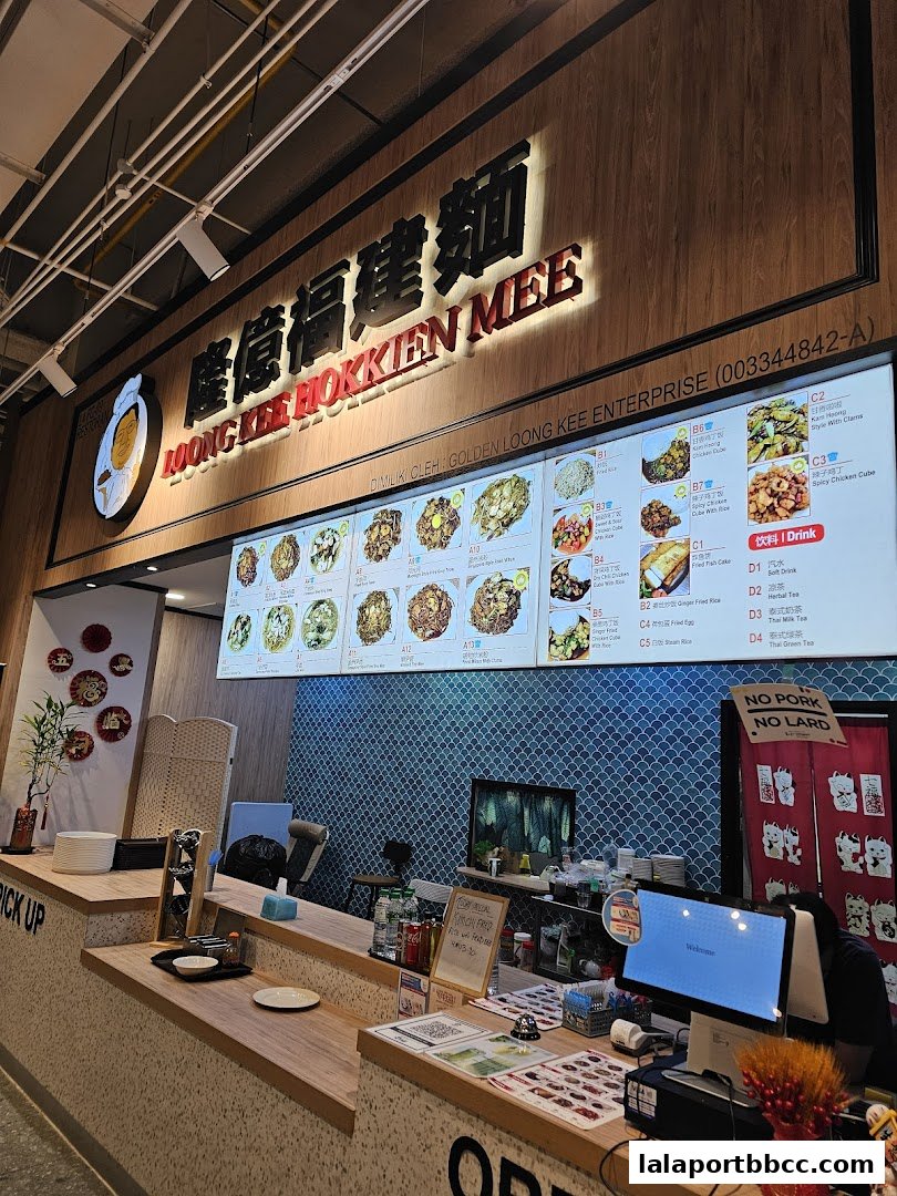 A food court stall with a large digital menu displaying various noodle dishes and drinks.