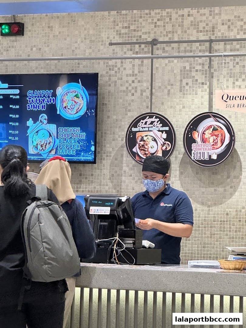 Customers queue at a counter with a digital menu displaying claypot dishes and a staff member serving.