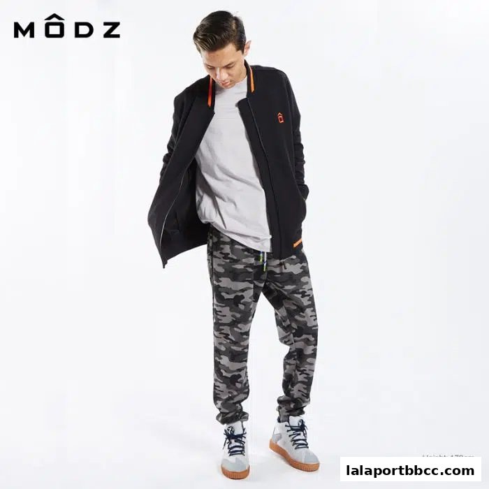 A young man models a black bomber jacket and camouflage pants from MODZ.