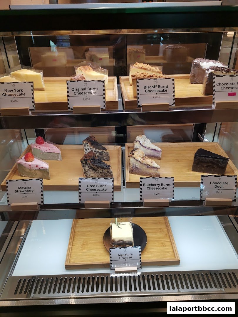 A display case filled with various cheesecakes and a tiramisu, each with a price label.
