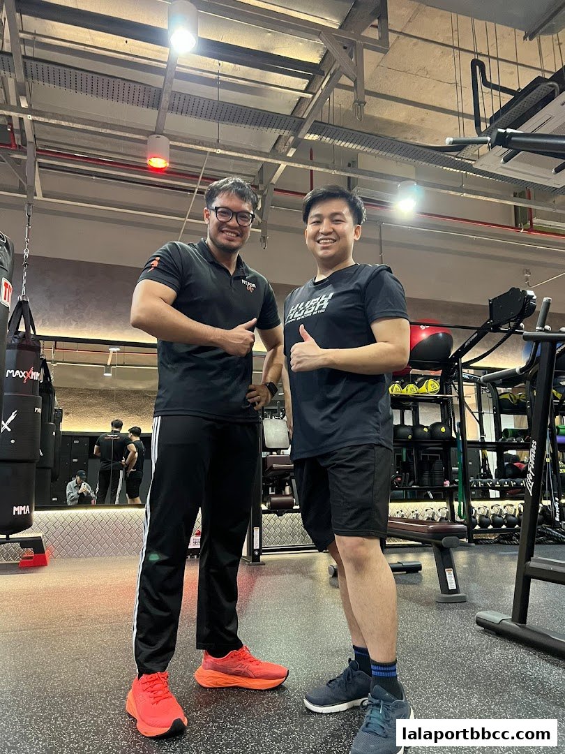 Two men giving thumbs up in a gym with fitness equipment.