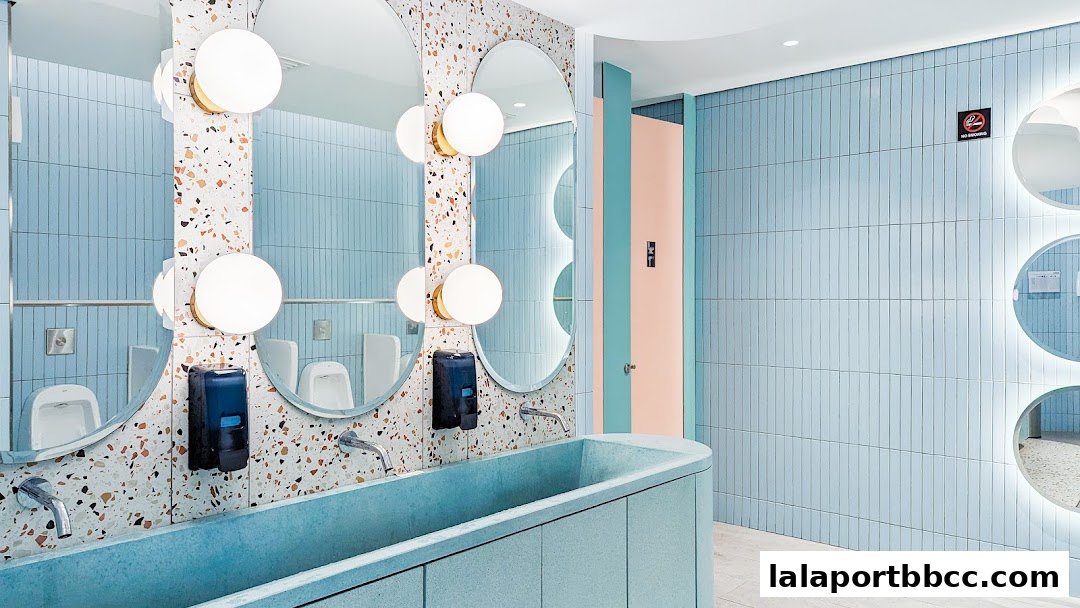 A stylish and modern restroom with blue tiled walls, terrazzo accents, and unique circular mirrors.