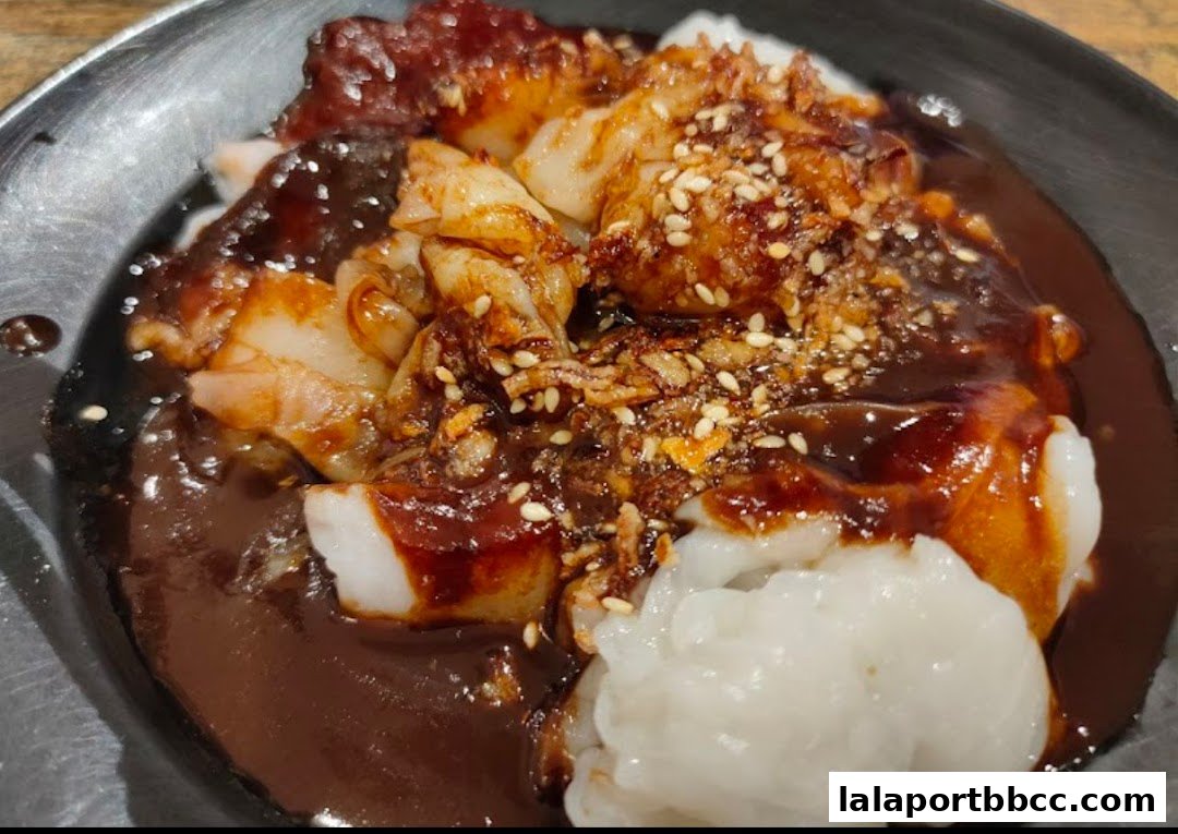 A close-up of delicious chee cheong fun with a rich, savory sauce and sesame seeds.