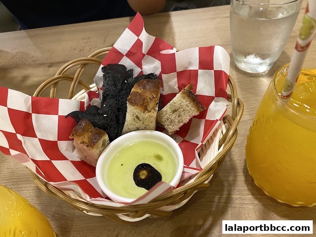A basket of assorted bread slices with olive oil dip and a glass of orange juice.