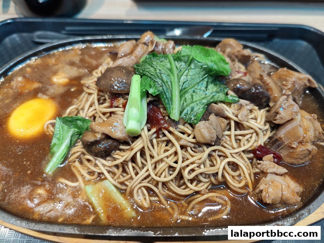 A sizzling hot plate of noodles with chicken, mushrooms, and a fried egg.