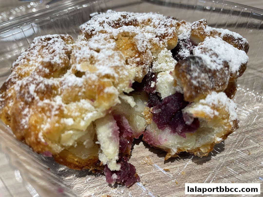A close-up of a pastry filled with purple fruit and dusted with powdered sugar.